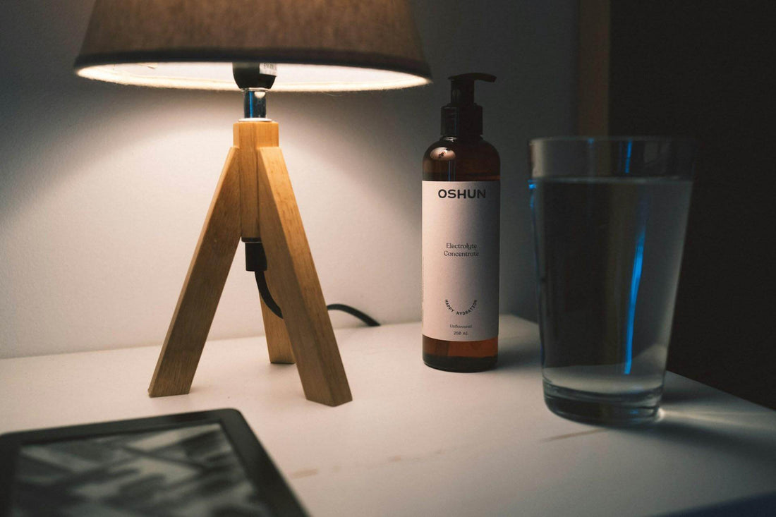 Stylish bedside setup with a wooden lamp, a water glass, and OSHUN skincare product for health and wellness.