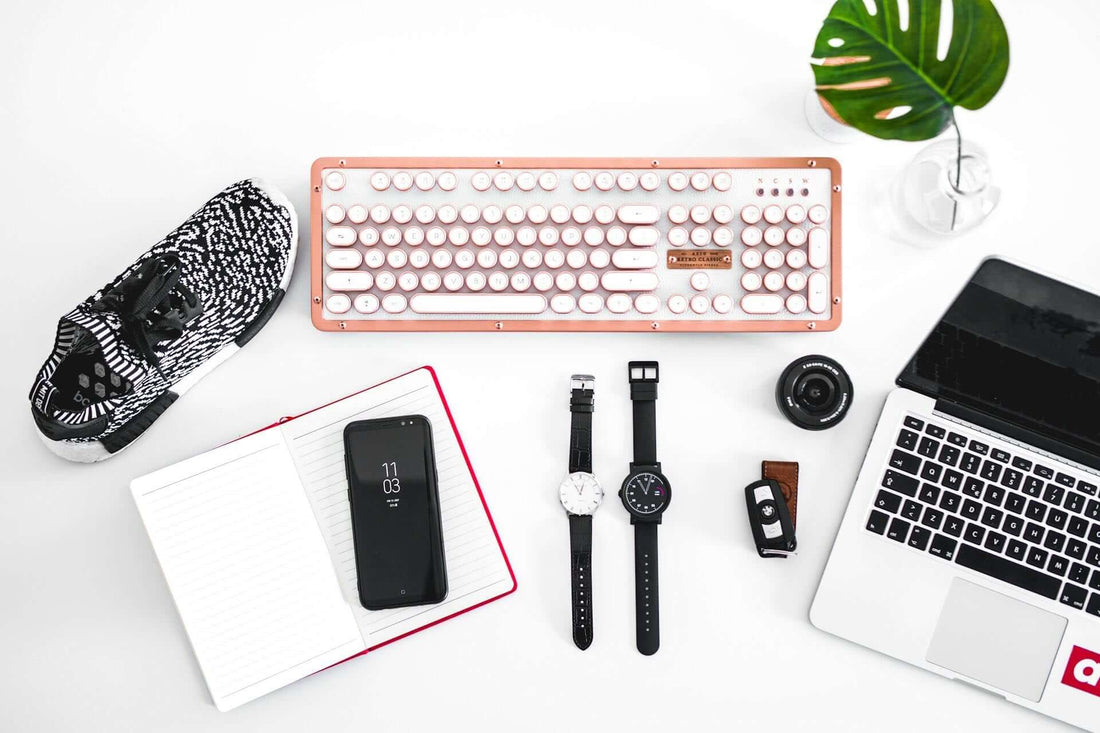 Stylish workspace with a vintage keyboard, smartwatch, sneakers, notebook, smartphone, and a laptop.