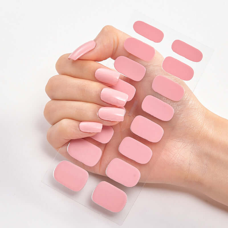 Hand holding pale pink Pure Color 16 nail stickers on clear backing, showcasing a stylish manicure.