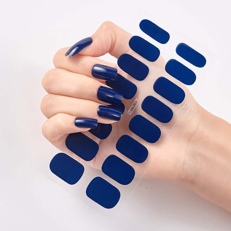 Close-up of hand with navy blue nail stickers, showcasing 16 solid color designs on transparent backing.