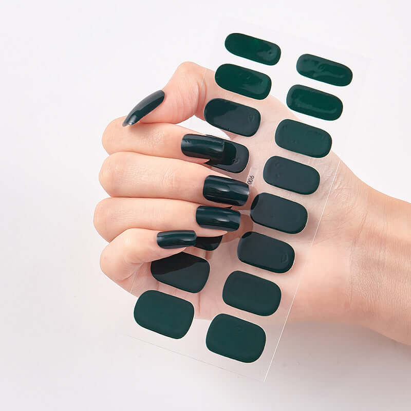 Hand holding Pure Color 16 Nail Stickers featuring dark green shades on nails for stylish manicures.