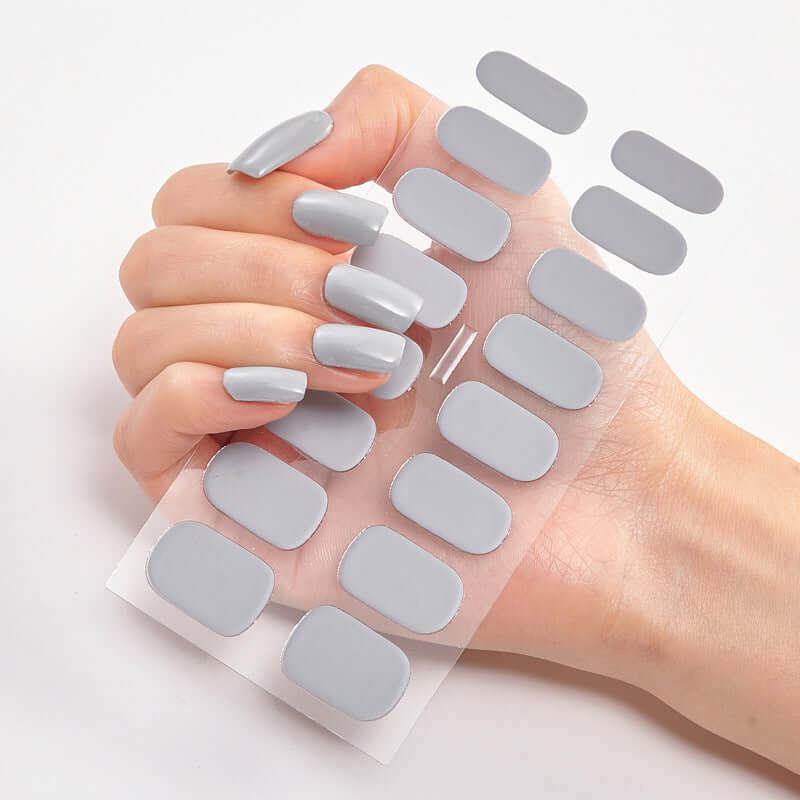 Hand displaying Pure Color 16 nail stickers in soft gray shades on a clear backing.
