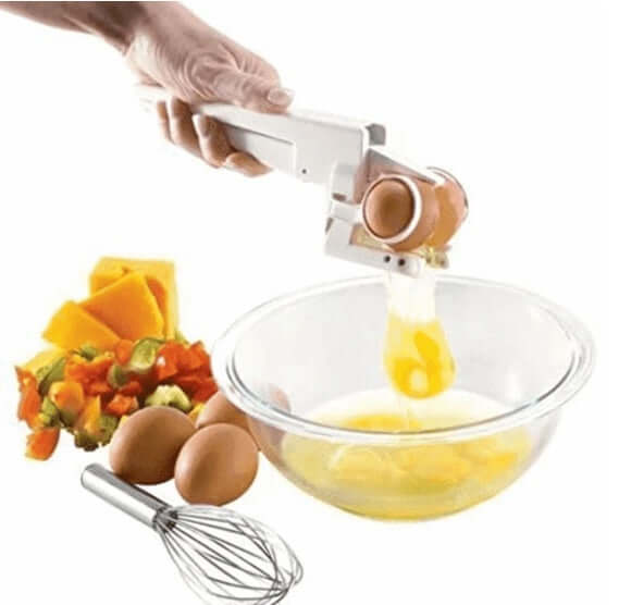 Handheld egg cracker tool breaking an egg into a bowl with vegetables and a whisk nearby for easy kitchen prep.