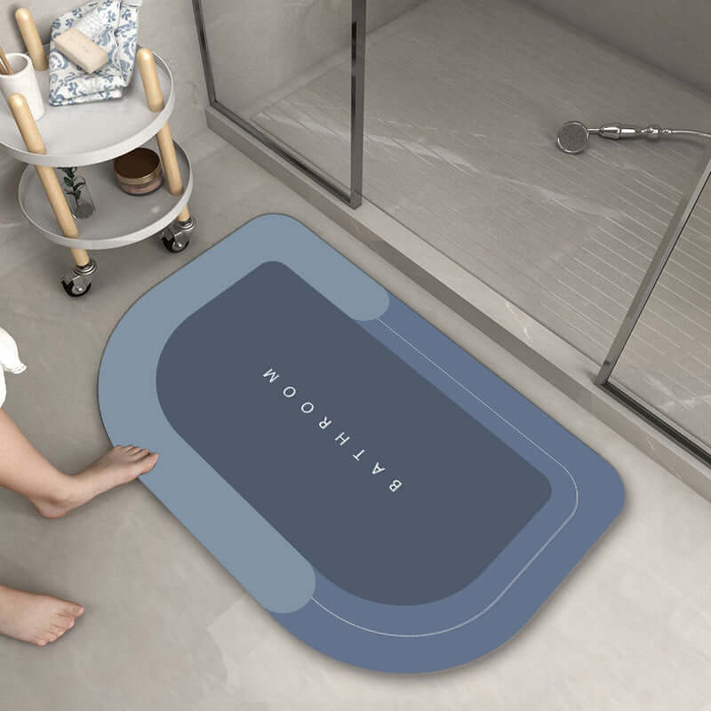 Modern oval bathroom mat in dark blue with the word 'BATHROOM', designed for absorbency and quick drying.