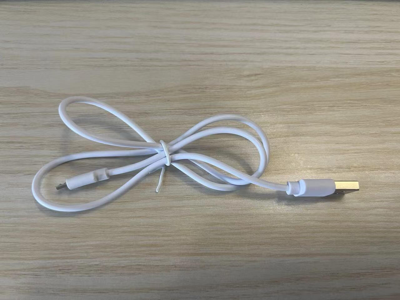 White USB charging cable on wooden surface, ideal for electronic devices and accessories.