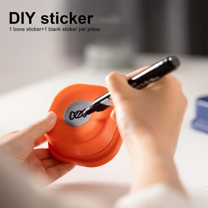 Close-up of a hand using a marker on an orange DIY sticker maker with a bone-shaped design.
