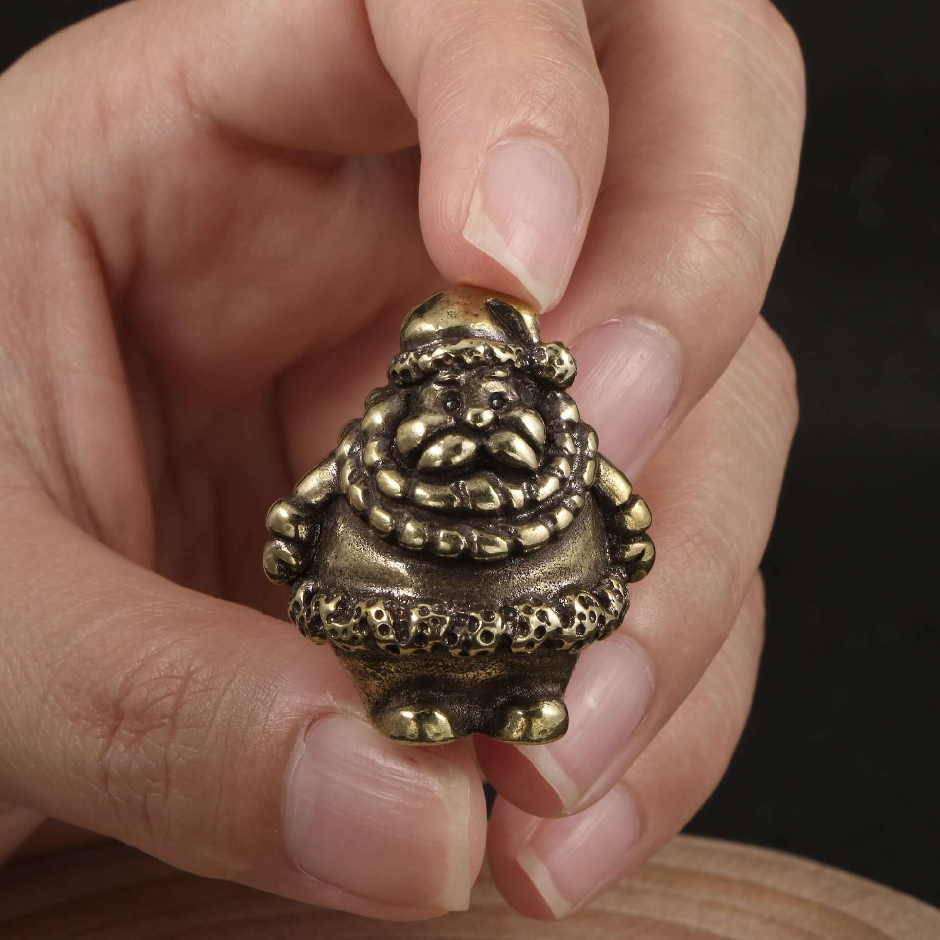 Hand holding a brass Santa figurine with detailed clothing and a joyful expression, perfect for Christmas decor.