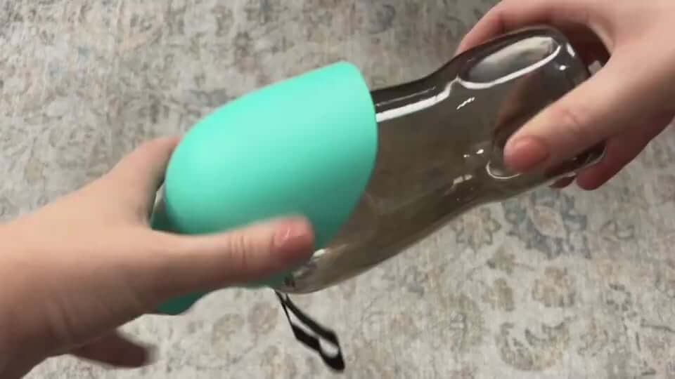 Hands holding a portable dog water bottle with a teal silicone cover, showcasing its design and usability.
