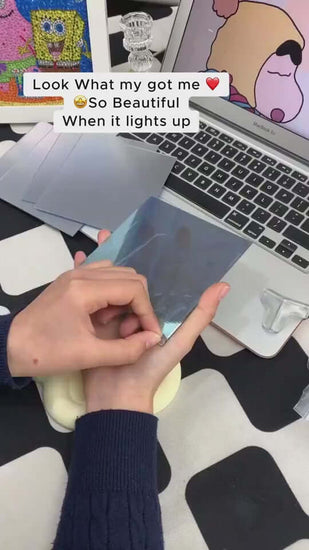 Person holding a shiny blue mirror sheet, with a laptop and colorful art in the background, showcasing DIY decor.