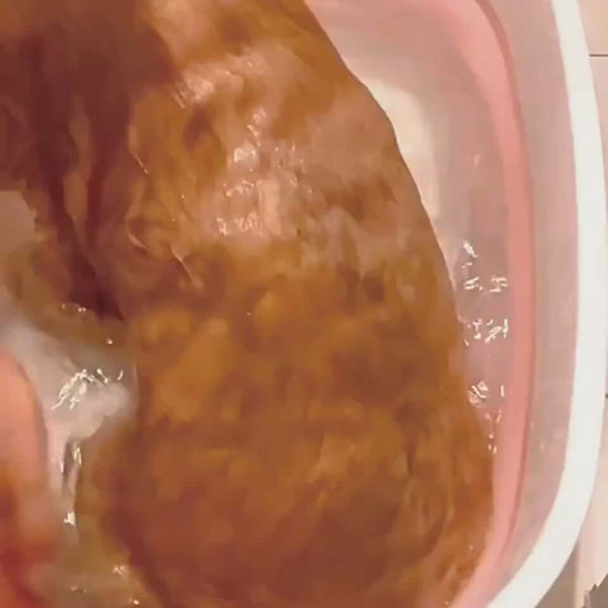 Golden dog being bathed with a gentle pet grooming brush in a pink tub.