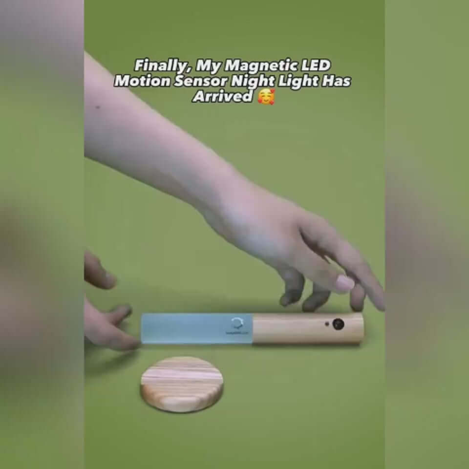 Hand placing a magnetic LED motion sensor night light on a wooden base against a green background.