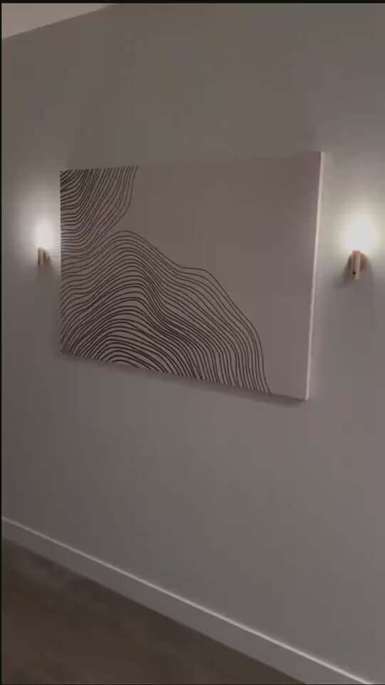 Stylish wall art with wavy lines illuminated by modern wall-mounted lights in a minimalist corridor.